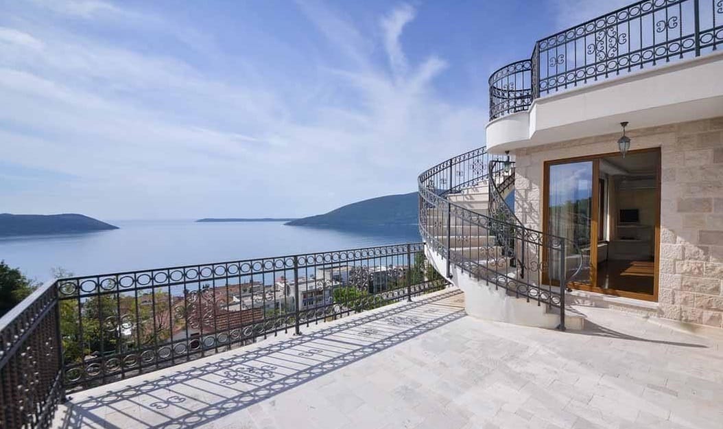 Przestronny taras willi w Herceg Novi, Czarnogóra, z kutą balustradą, spiralnymi schodami i panoramicznym widokiem na morze.