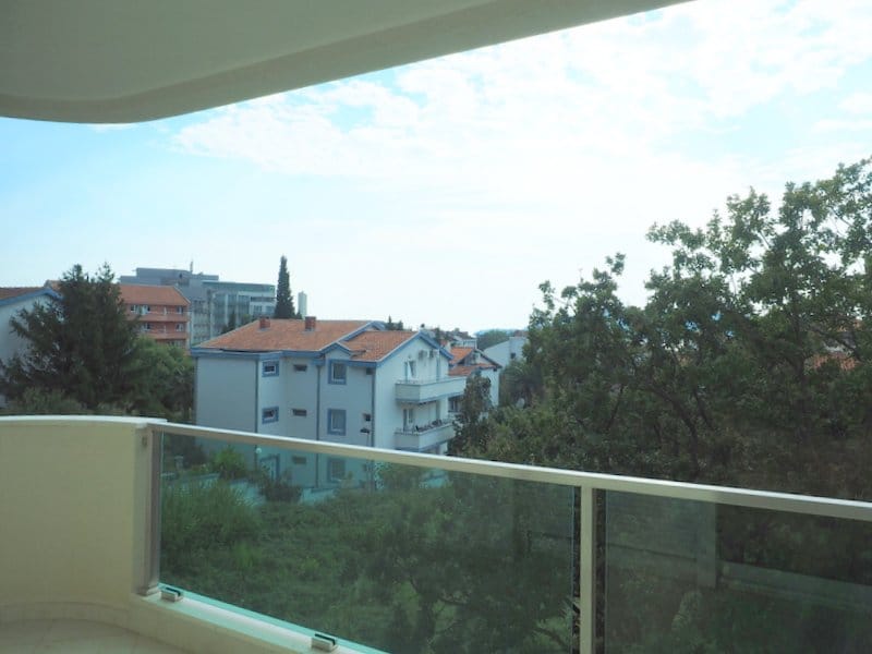 Pogled sa balkona stana u Bečićima, Crna Gora: panorama zelenih stabala i stambenih zgrada sa krovovima od crepova.