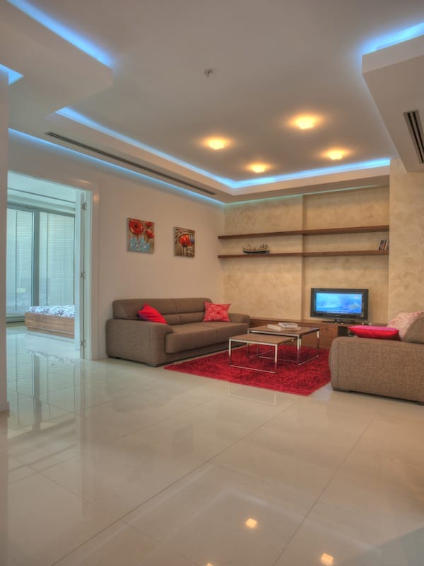 Modernes Wohnzimmer in einer Wohnung in Budva, Montenegro: beige Möbel, roter Teppich, Deckenbeleuchtung und Fliesen.