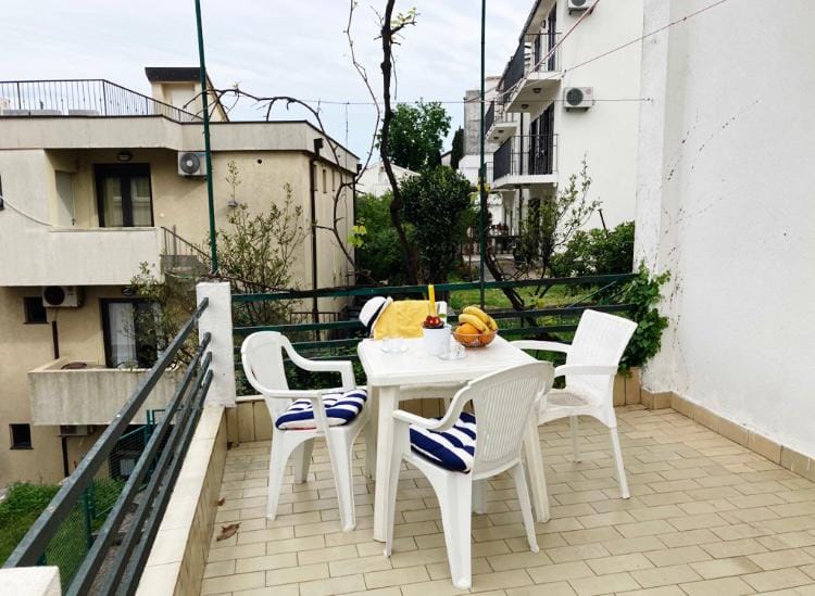 Ugodna terasa s plastičnim nameštajem i pogledom na grad u hotelu u Budvi, Crna Gora. Balkon s pločicama i zelenilom.
