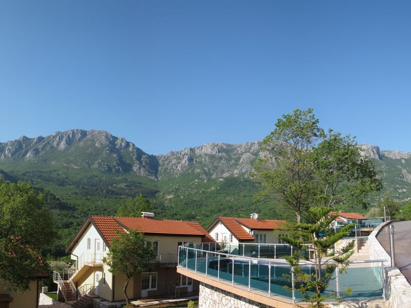 View of a residential complex with a pool and panoramic mountains in Bar, Montenegro. Modern houses with tiled roofs.