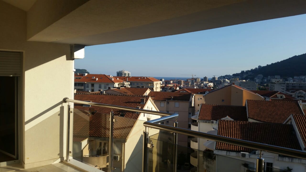 Pogled sa balkona stana u Budvi, Crna Gora: panorama grada sa krovovima od crepa i morskim horizontom.