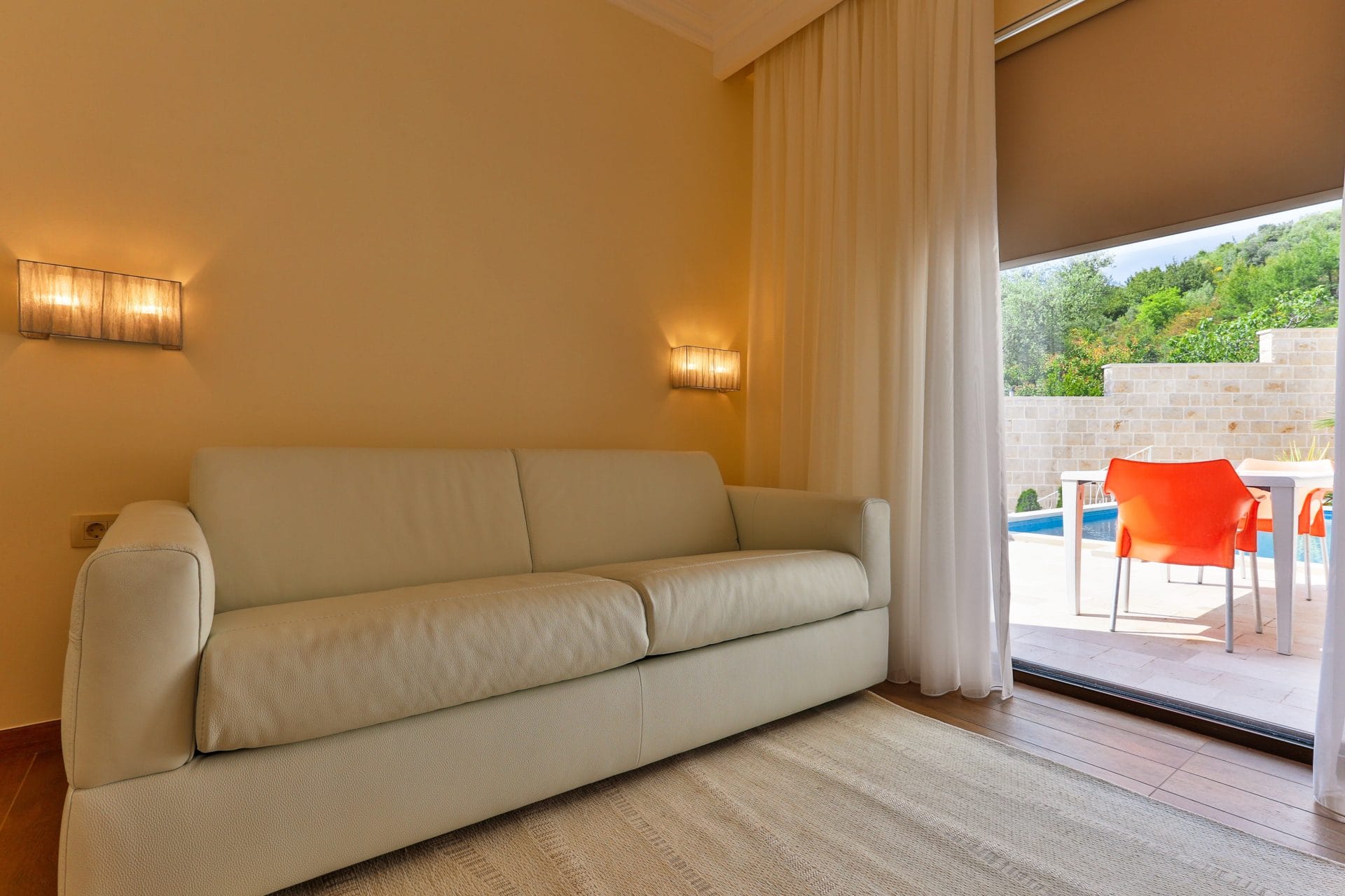 Villa living room in Tivat, Montenegro: a light leather sofa, access to the terrace with a pool and garden view.