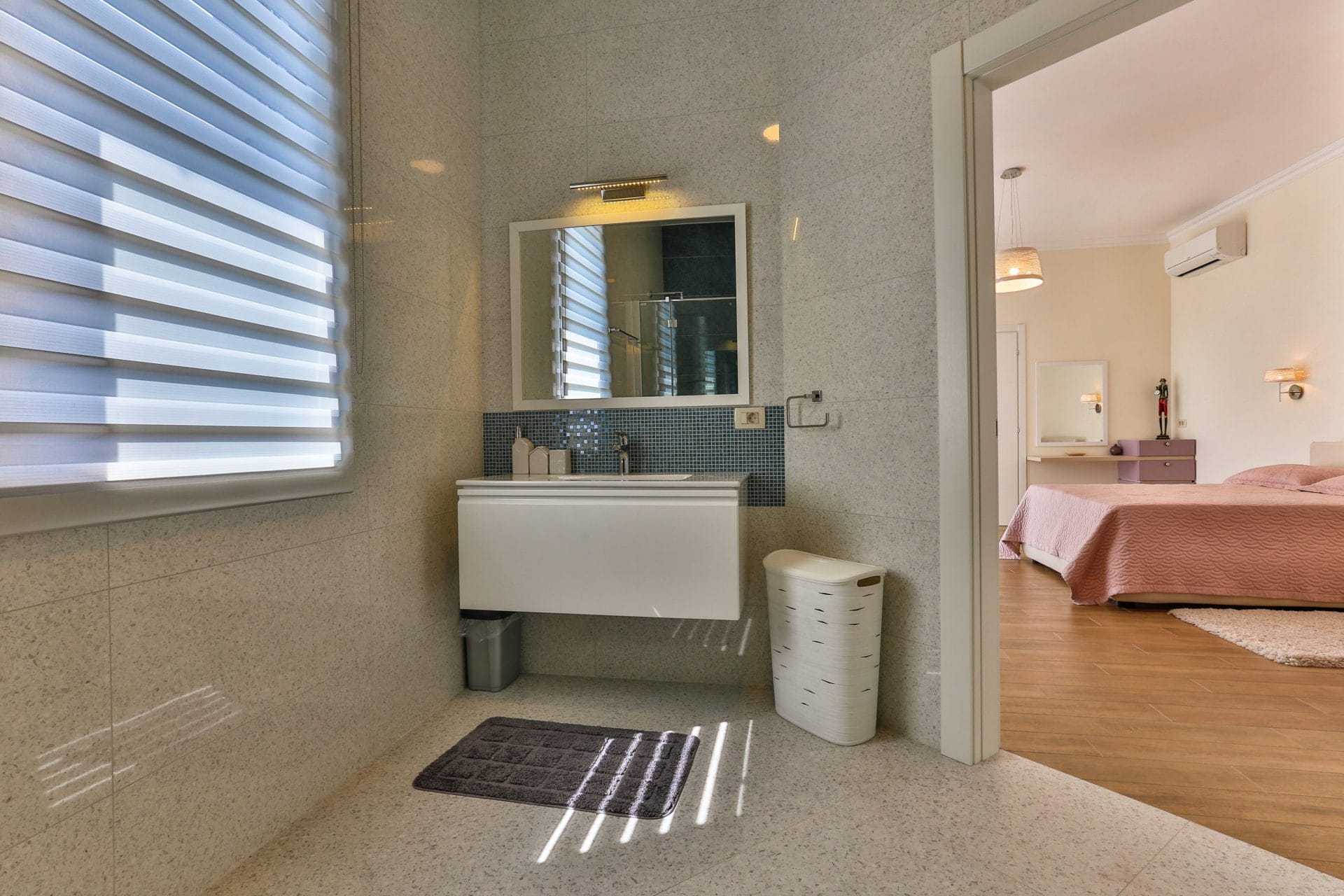 Modern bathroom with white furniture and a view of the bedroom in a villa in Tivat, Montenegro. Light tiles and decor.
