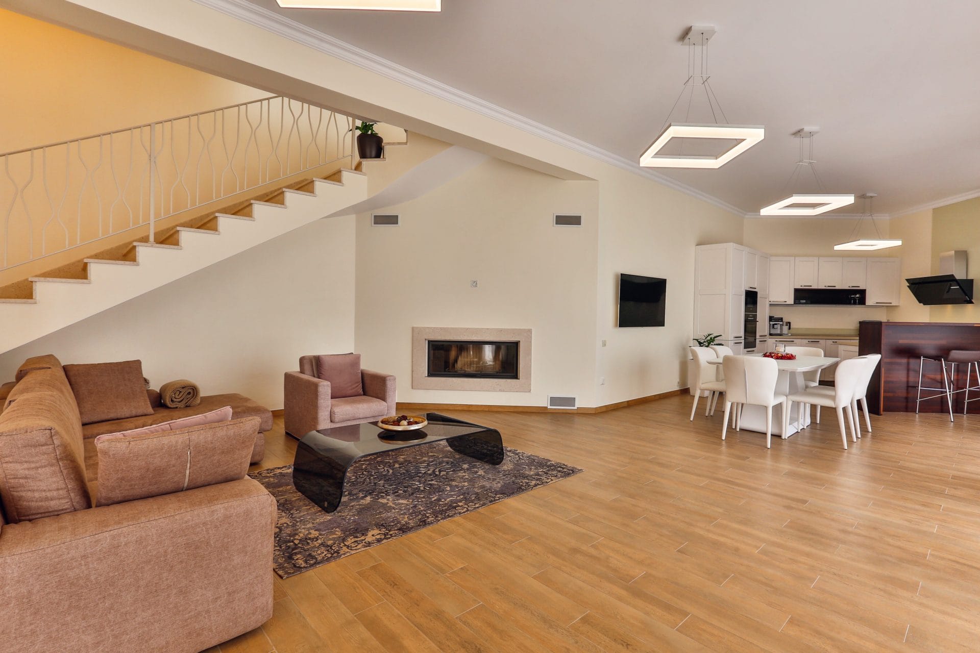 Spacious living room with a fireplace and kitchen in a villa in Tivat, Montenegro: modern furniture, staircase, and bright interior.