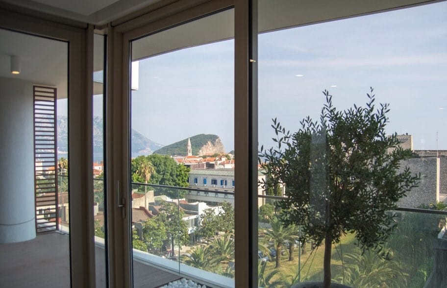 Pogled iz panoramskih prozora dnevne sobe na Stari grad i more u Budvi, Crna Gora: savremen enterijer i terasa.