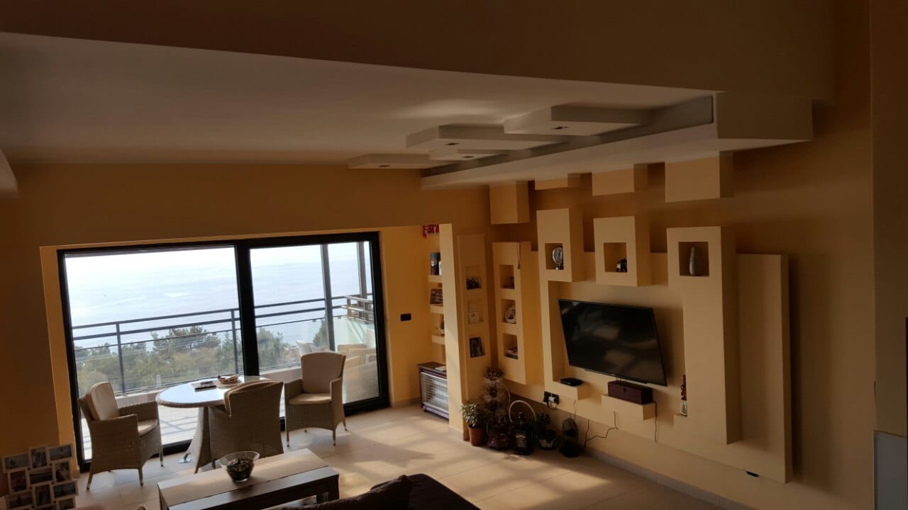Dnevna soba u kući u Šušnju, Crna Gora: dizajnerski zid sa TV-om, panoramski prozori i terasa s pogledom na more.