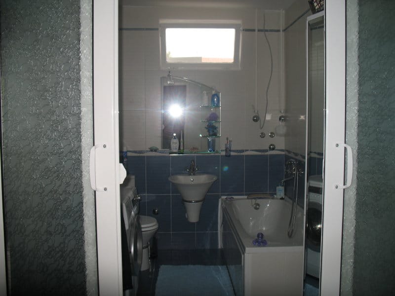 Kupatilo u kući u Šušnju, Crna Gora: plave pločice, kada, lavabo, ogledalo i veš mašina.