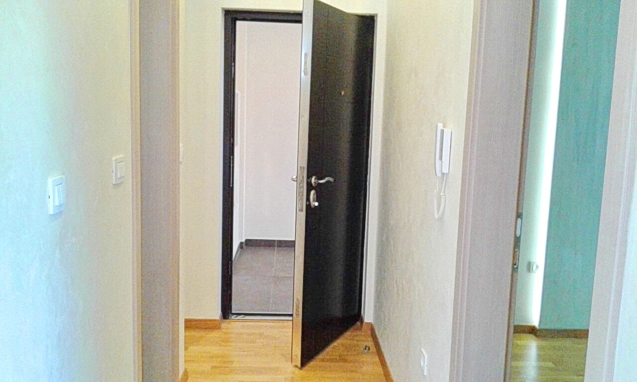 Predsoblje sa tamnim ulaznim vratima i svetlom oblogom u stanu, Bečići, Crna Gora: pogled na hodnik i unutrašnja vrata.
