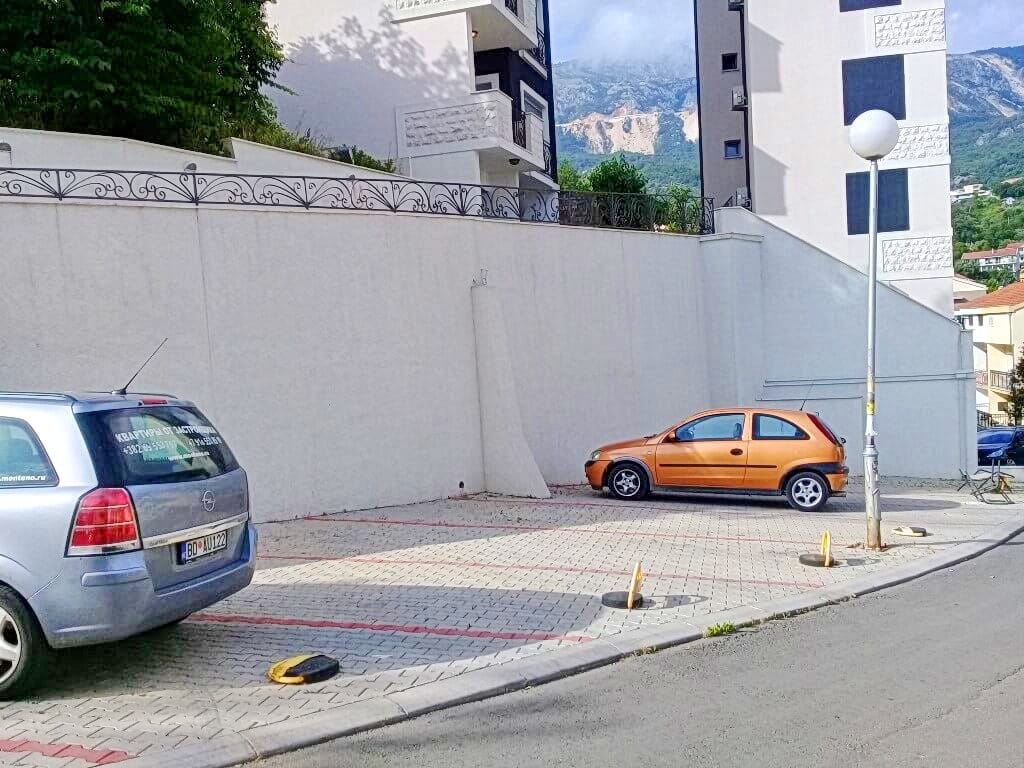 Parking kod stambene zgrade u Bečićima, Crna Gora, sa pogledom na planine i označenim mestima za automobile stanara.