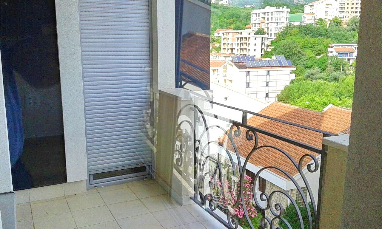 Balkon sa kovanom ogradom i pogledom na grad Bečići, Crna Gora, u modernom stanu sa zaštitnim roletnama.