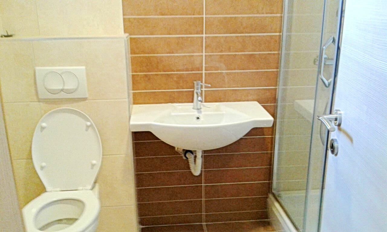 Kupatilo u stanu u Bečićima, Crna Gora: tuš kabina, viseća WC šolja i umivaonik sa bež pločicama.