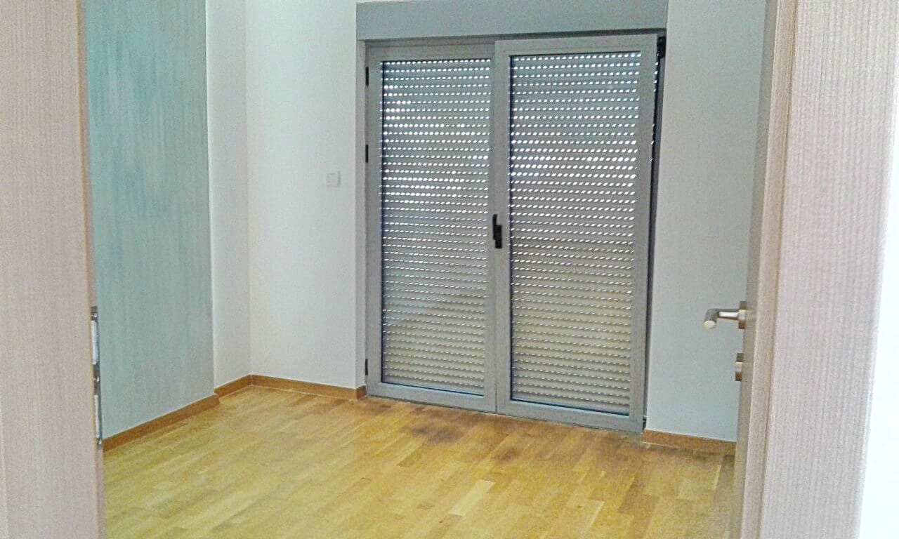 Svetla spavaća soba u stanu u Bečićima, Crna Gora: parketni pod, panoramska vrata sa zaštitnim roletnama.