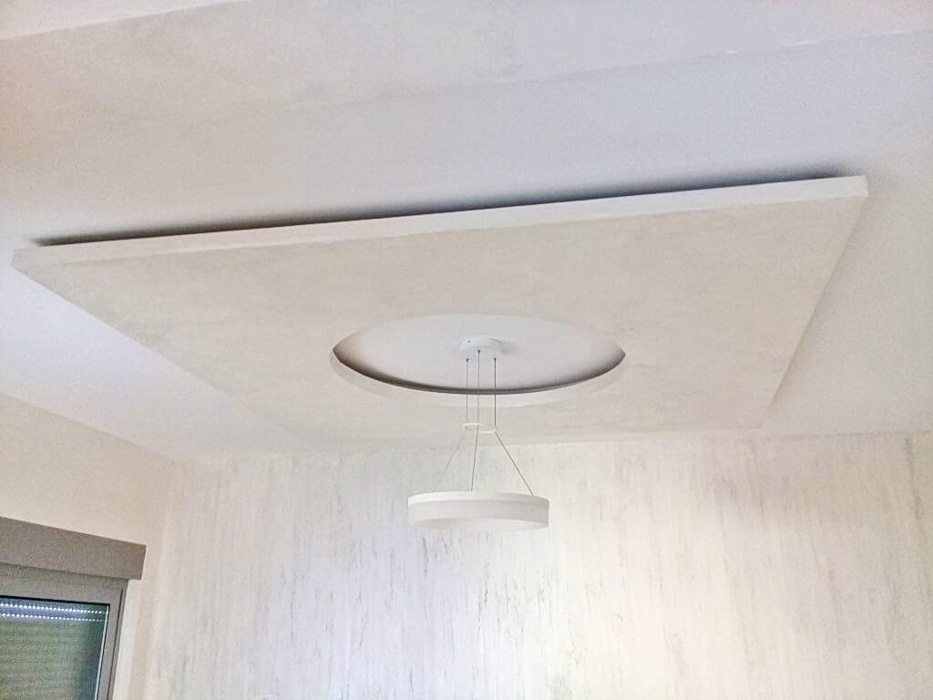 Moderan dizajn plafona sa kružnom nišom i lusterom u dnevnoj sobi stana u Bečićima, Crna Gora. Zidovi su dekorativno obrađeni.