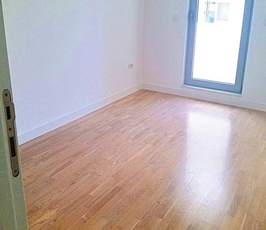 Svetla prazna spavaća soba sa parketnim podom i izlazom na balkon u stambenom kompleksu u Budvi, Crna Gora.