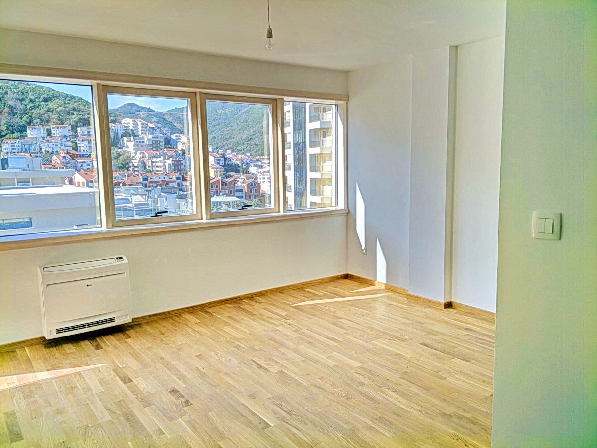 Svetao dnevni boravak sa parketom i panoramskim pogledom na planine i grad Budvu, Crna Gora, u modernom stanu.