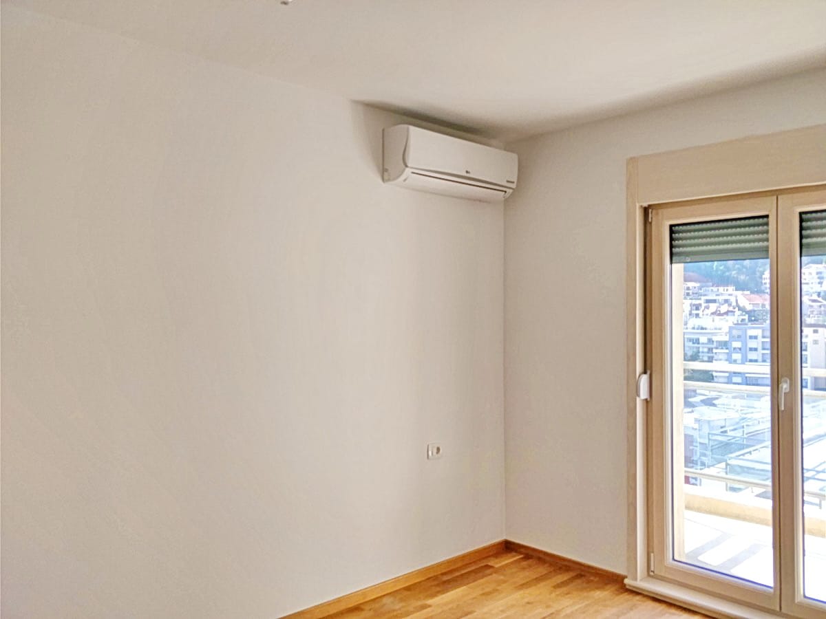 Osvetljena dnevna soba sa klima-uređajem i izlazom na balkon u stanu, Budva, Crna Gora. Parketni pod, pogled na grad.