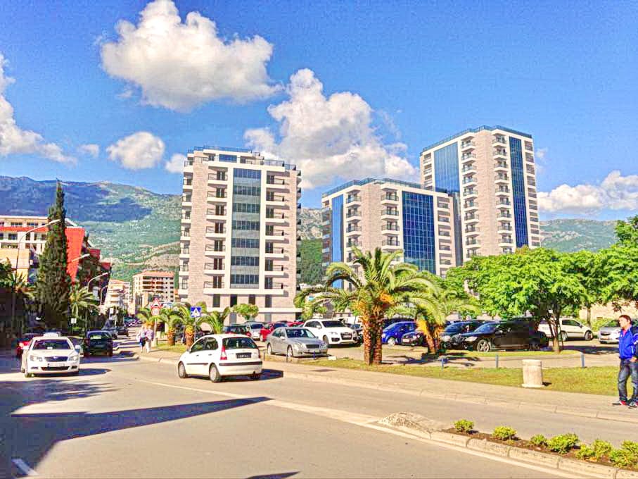 Savremeni stambeni kompleksi u Budvi, Crna Gora: pogled na višespratnice sa panoramskim prozorima i planinski pejzaž.