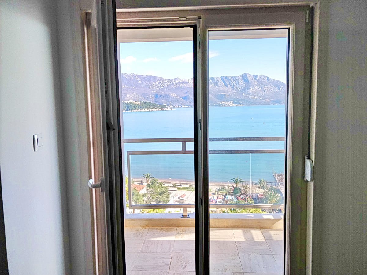 Pogled iz spavaće sobe na more i planine sa balkona stana u Budvi, Crna Gora: panoramski prozori i svetla završna obrada enterijera.