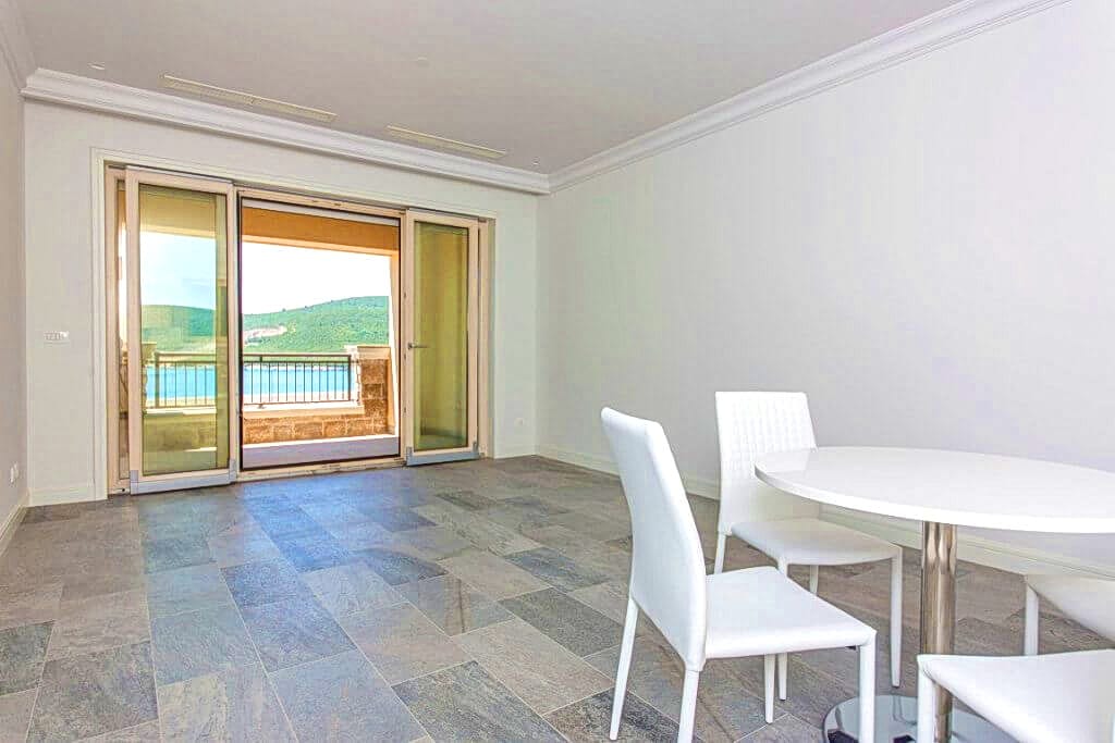 Dnevna soba sa belim nameštajem i izlazom na terasu s pogledom na more u stanu, Luštica, Crna Gora.