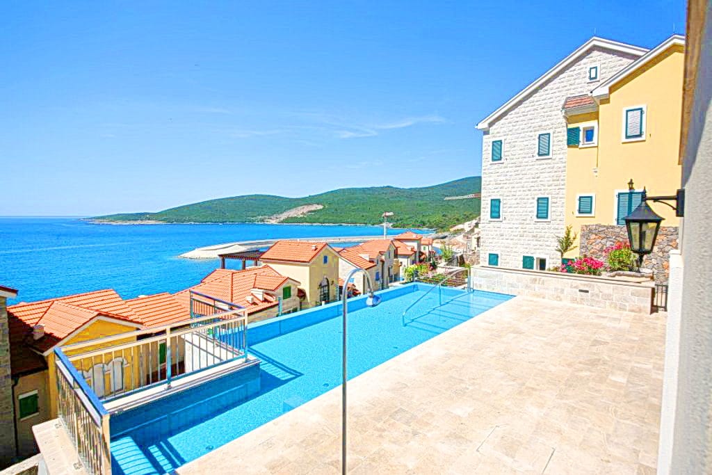 Bazen s pogledom na more i vile u Luštica Bayu, Crna Gora: terasa sa kamenim oblogama i panoramski morski pejzaž.