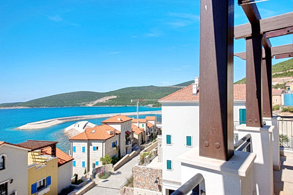 Pogled sa balkona na more i kompleks Lustica Bay u Crnoj Gori: mediteranska arhitektura, krovovi od crepova i planine.
