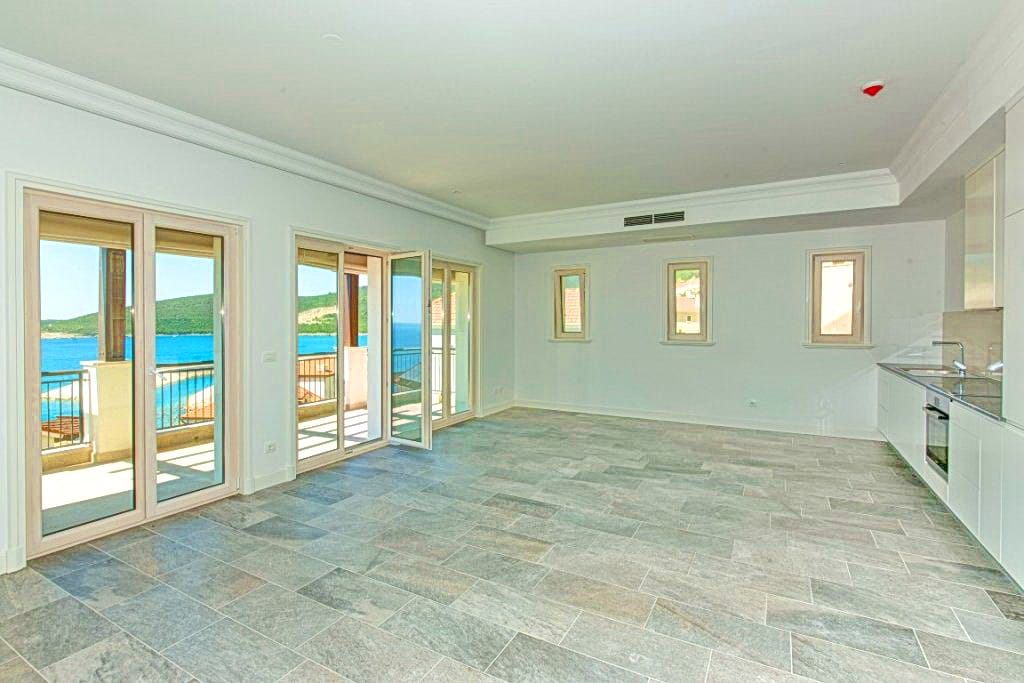 Svetla dnevna soba sa kuhinjom i panoramskim pogledom na more u stanu na Luštici, Crna Gora. Kameni pod, moderan dizajn.