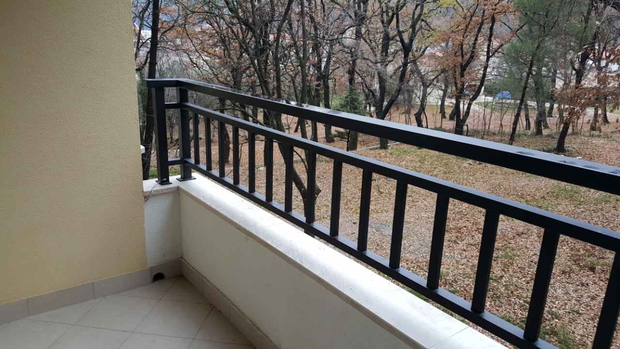 Balkon sa crnim metalnim ogradama i pogledom na šumski park u stanu u Budvi, Crna Gora.