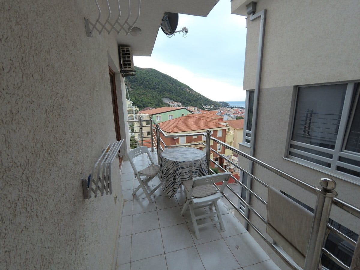 Balkon sa nameštajem i pogledom na planine i more u stanu u Budvi, Crna Gora. Svetla završna obrada i pločice na podu.