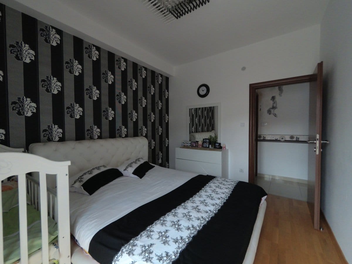 Bedroom in an apartment in Budva, Montenegro: double bed, accent wall with wallpaper, dresser, and crib.