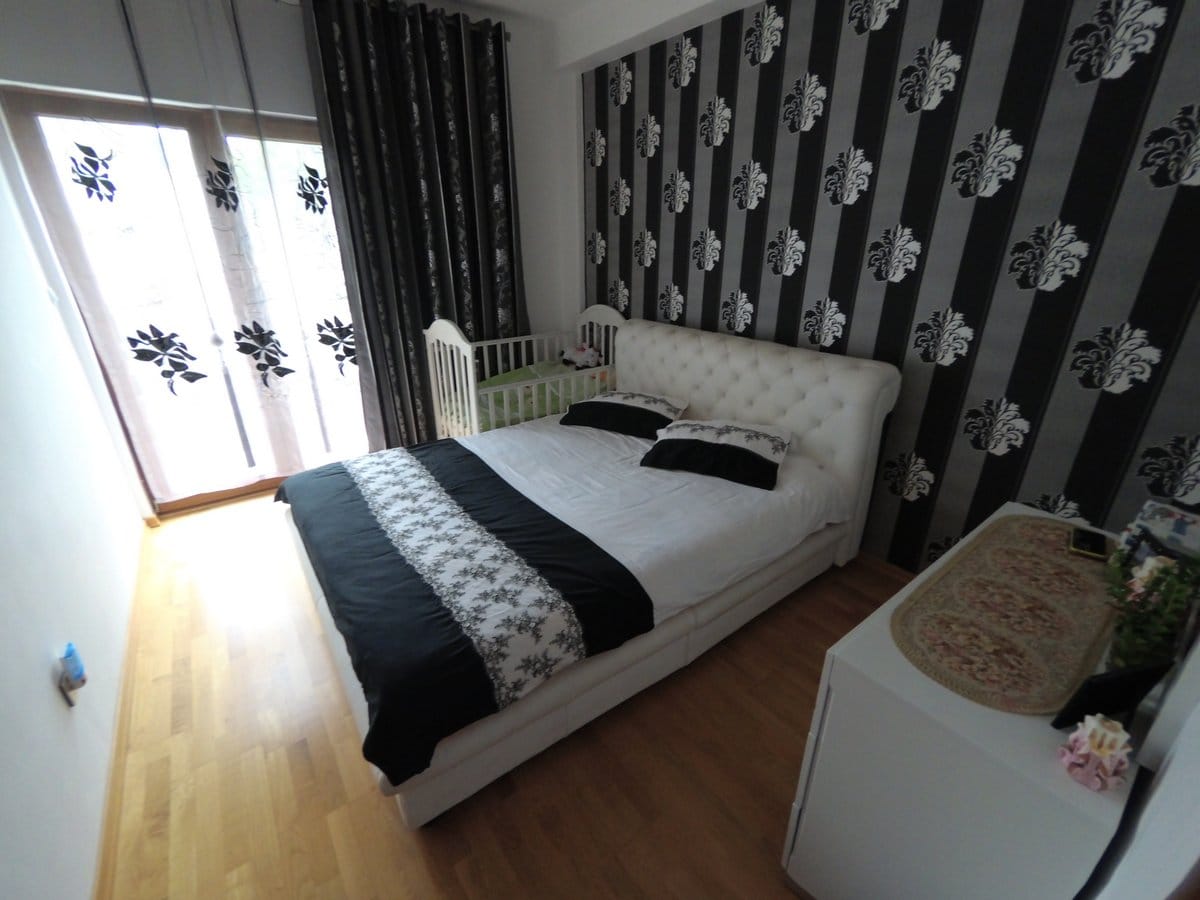 Bedroom in an apartment in Budva, Montenegro: a double bed, a crib, striped wallpaper, and access to the balcony.