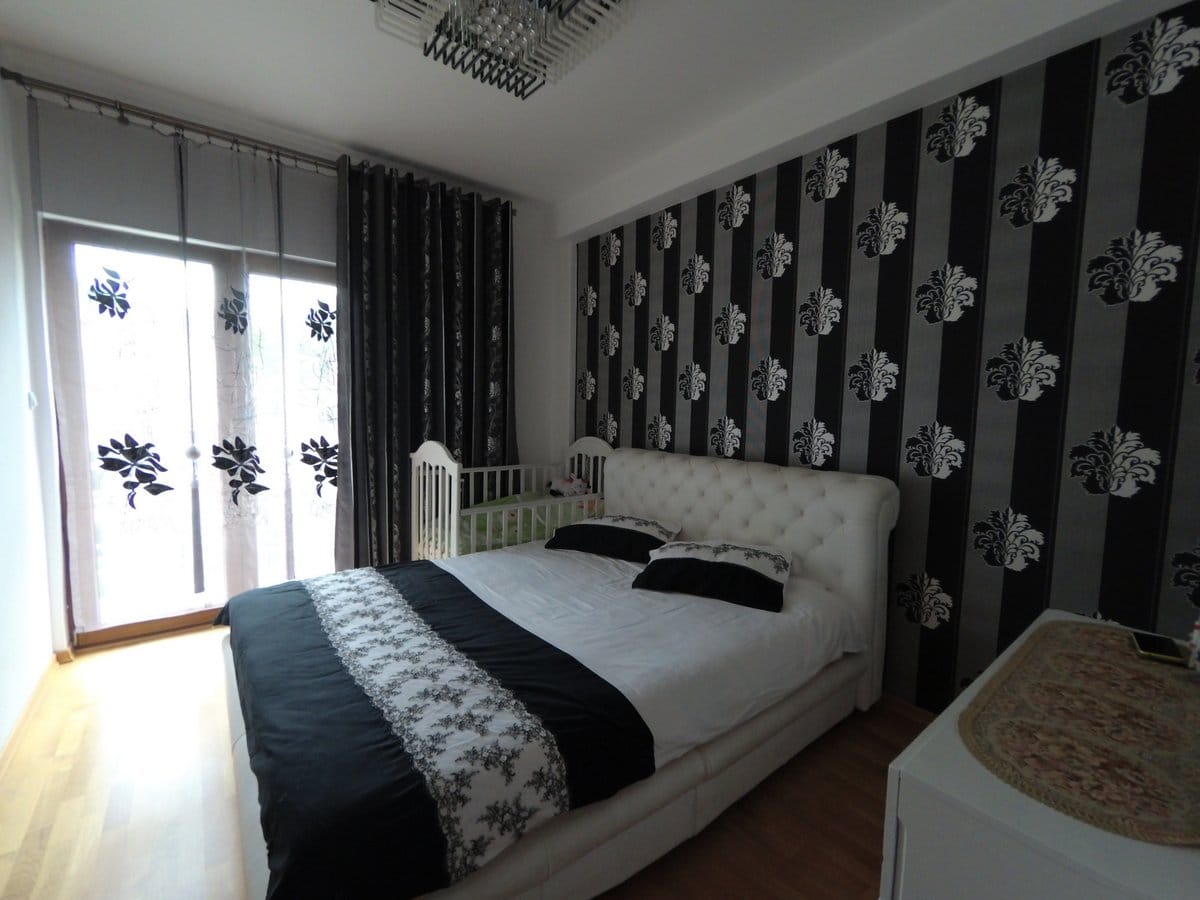 Bedroom in an apartment in Budva, Montenegro: a double bed, a crib, and an accent wall with wallpaper.