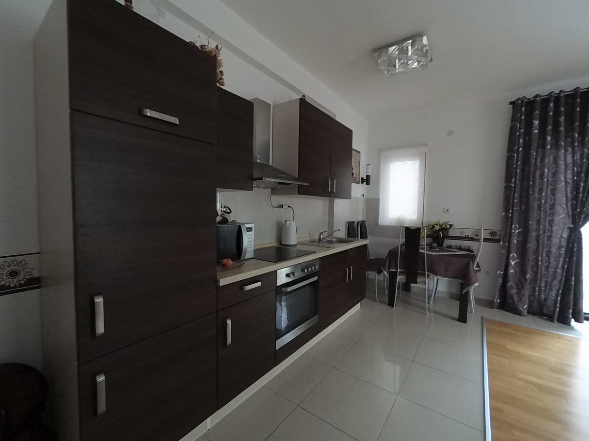 Modern kitchen with dark cabinetry and a dining area in an apartment in Budva, Montenegro. Light flooring and tile.