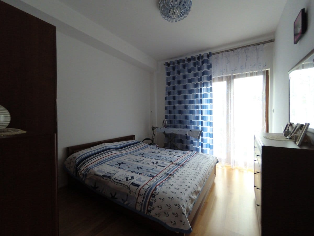 Cozy bedroom with a double bed in an apartment in Budva, Montenegro: bright interior, parquet flooring, and access to the balcony.