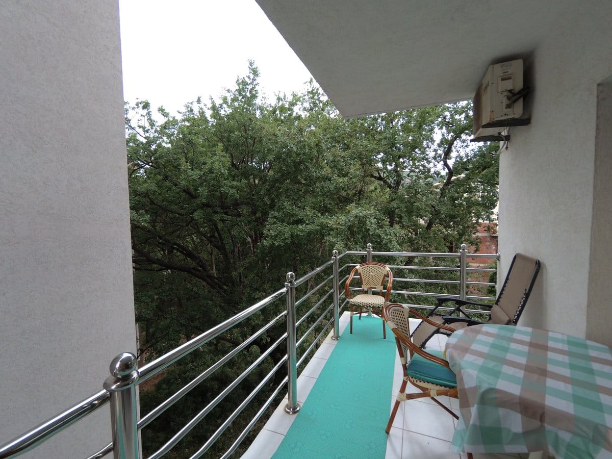 Cozy balcony with furniture and a view of greenery in an apartment in Budva, Montenegro: table, chairs, and metal railing.
