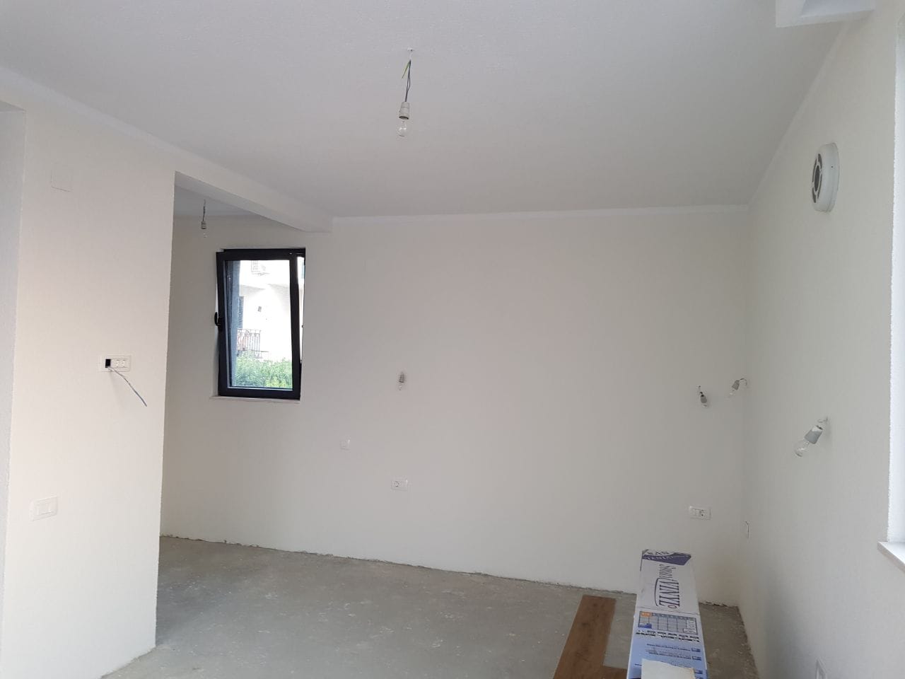 Dnevna soba u procesu renoviranja u vili u Krašićima, Crna Gora: beli zidovi, betonski pod i panoramski prozor.