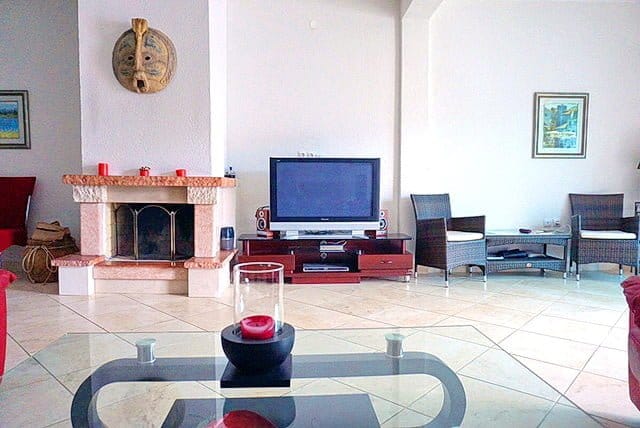 Living room with a fireplace, TV area, and wicker furniture in an apartment, Stoliv, Montenegro. Interior with tiled flooring.