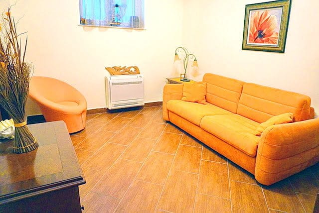 Cozy living room with an orange sofa and armchair in an apartment in Stoliv, Montenegro: tiled floor and light finishes.