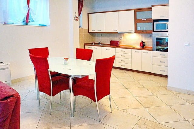 Kitchen-dining room with white cabinetry and red chairs in an apartment for sale, Stoliv, Montenegro.