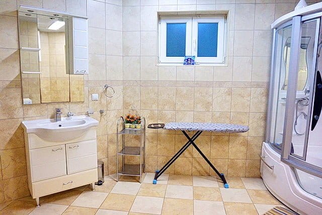 Bathroom in an apartment in Stoliv, Montenegro: shower cabin, vanity with sink, mirror, and ironing board.