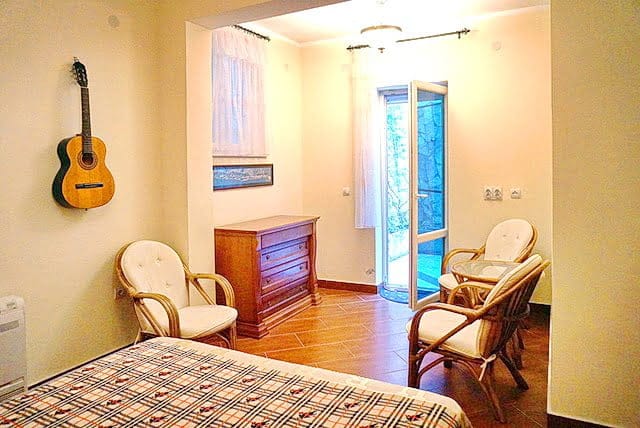Cozy bedroom in an apartment, Stoliv, Montenegro: wicker chairs, a wooden dresser, a guitar on the wall, and access to the terrace.