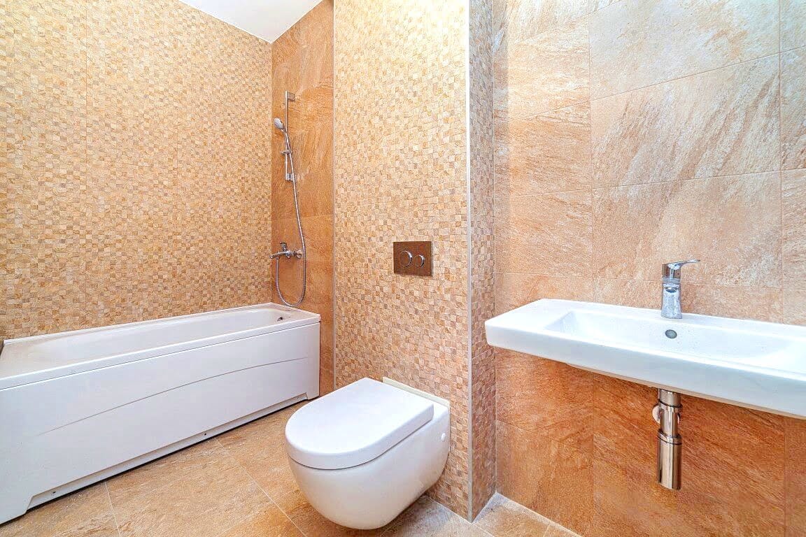 Savremeno kupatilo sa belom sanitarnom opremom i bež pločicama u stanu, Kotor, Crna Gora.