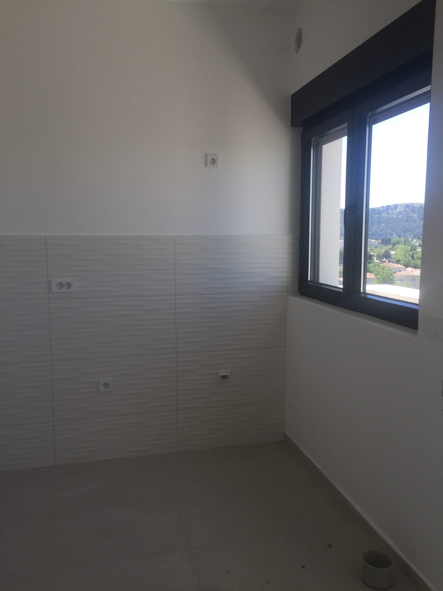 Neue Küche in einer Wohnung in Bar, Montenegro: helle Fliesenverkleidung, Panoramafenster mit Blick auf die Berge und die Stadt.