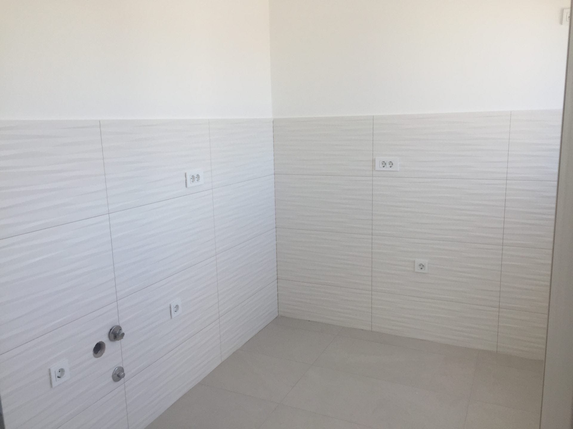 Küchenbereich in einer neuen Wohnung in Bar, Montenegro: helle Fliesen, Anschlüsse für Versorgungsleitungen und Steckdosen für die Küchenzeile.