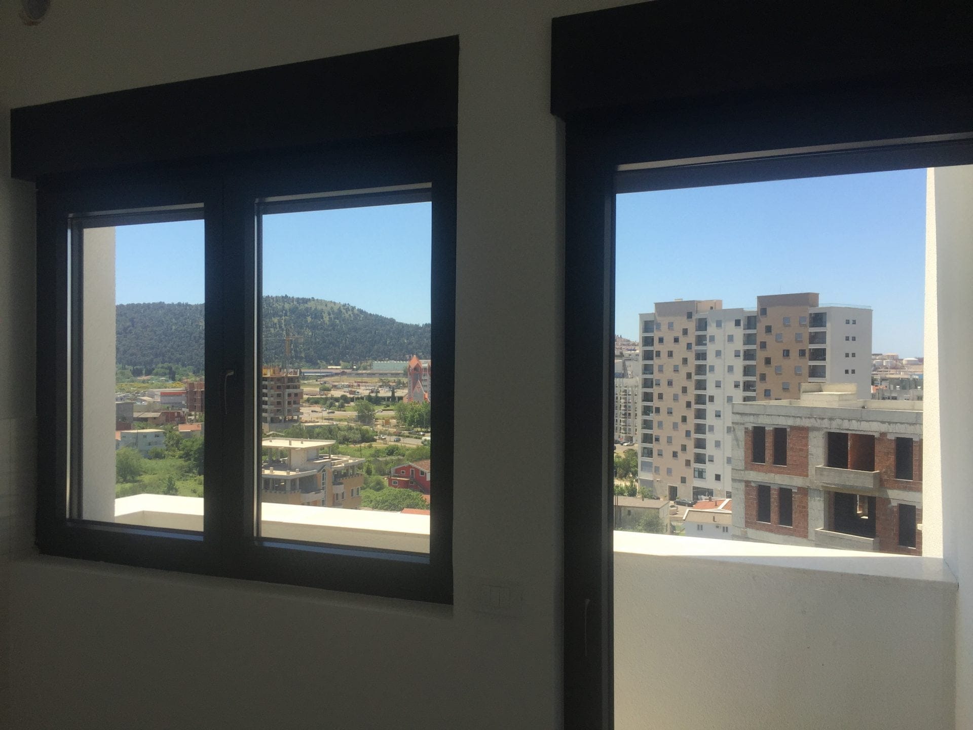Blick aus dem Wohnzimmerfenster auf die Stadt und die Berge in einer Wohnung, Stadt Bar, Montenegro. Moderne Fenster mit dunklem Rahmen.