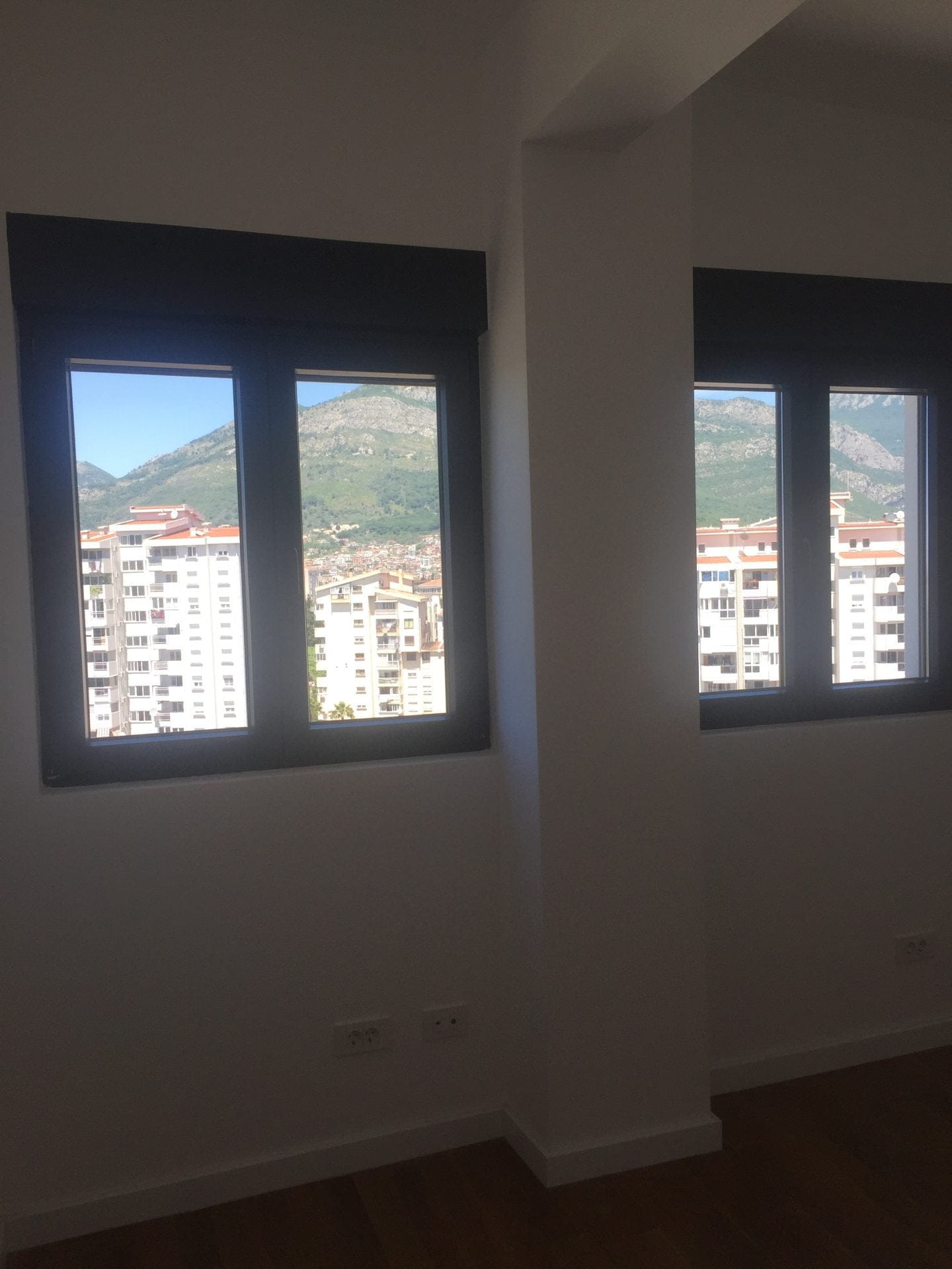 Helles Wohnzimmer mit Panoramablick auf die Berge und die Stadt Bar, Montenegro, durch moderne Fenster mit dunklem Profil.