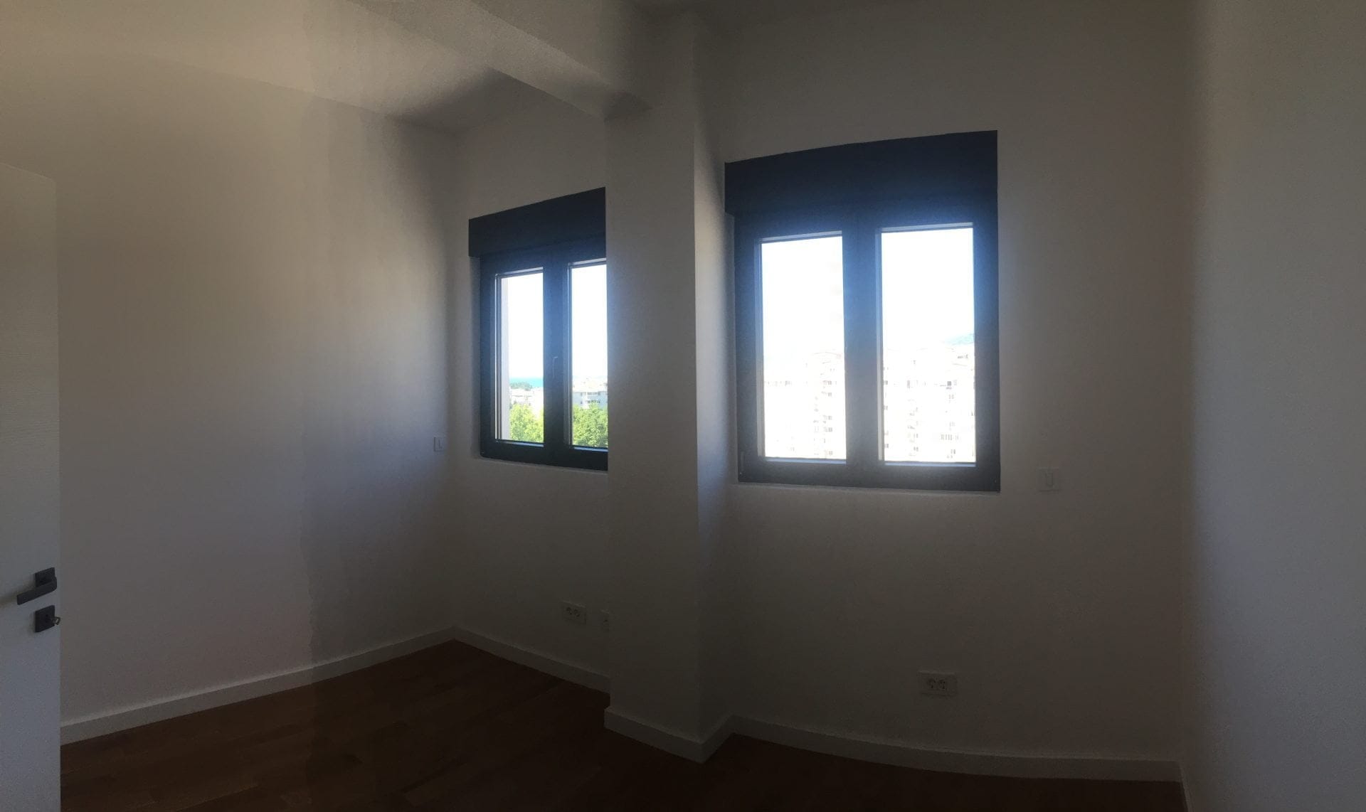 Helles Schlafzimmer mit Parkett und Panoramafenstern in einer Wohnung in der Stadt Bar, Montenegro. Blick auf die Stadt und das Grün.