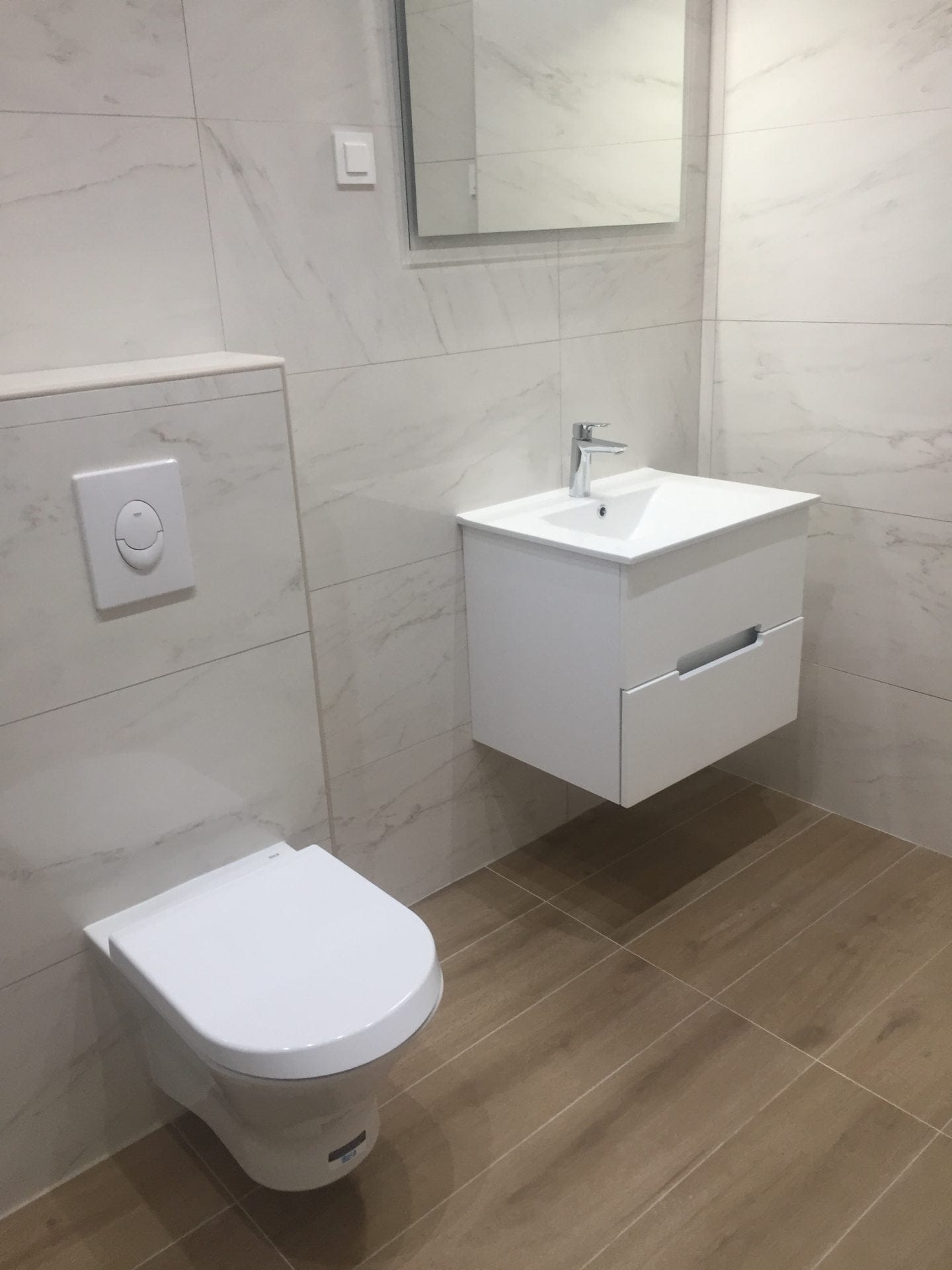 Modernes Badezimmer in einer Wohnung, Stadt Bar, Montenegro: hängender Waschtischunterschrank, Vorwandelement und Marmoroptik-Fliesen.
