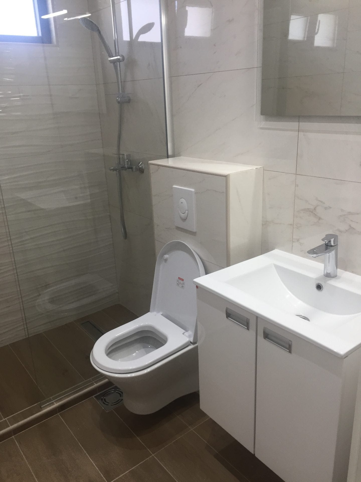 Modernes Badezimmer in einer Wohnung in Bar, Montenegro: Duschkabine, helle Fliesen und weiße Sanitärkeramik.