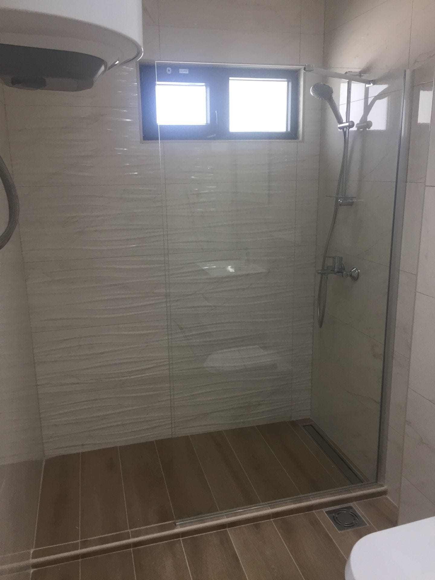 Moderne Duschkabine mit Fenster in einer Wohnung, Stadt Bar, Montenegro: helle Fliesen, Glasabtrennung und Dusche.